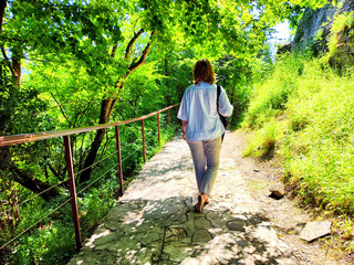 A woman strolls peacefully down a stone pathway enveloped by vibrant green foliage on a sunny day