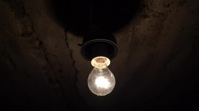 A light bulb in a dark basement blinks due to voltage drop.