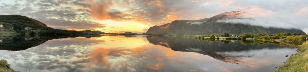 Panoramic view of Norway's Lofoten Islands under the midnight sun. Golden light illuminates mountains, coastlines, and calm waters, showcasing the stunning beauty of the Arctic summer landscape.