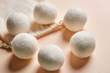 Six white wool dryer balls arranged around a cotton drawstring bag on a soft beige background. Eco-friendly, reusable laundry aid for reducing static and wrinkles