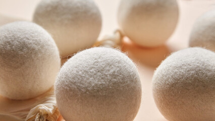 Close-up view of natural wool dryer balls with a cotton bag on a warm beige background....