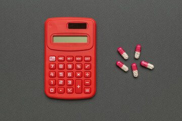 Red Calculator and Pink-White Capsules on Gray Background: Finance Meets Healthcare Concept