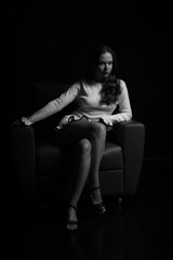 Low key black and white portrait of young woman sitting in a chair