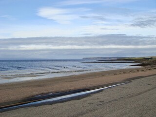 A peaceful coastline view showcasing distant cliffs under a vast blue sky, meeting a calm sea. The tranquil scene captures the serene atmosphere of nature, ideal for travel and outdoor photography.