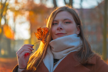Young woman enjoying autumn vibes in a park while holding a colorful leaf during sunset