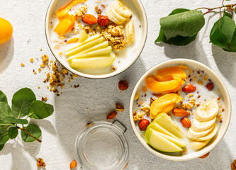 Breakfast bowl filled with crunchy granola, fresh slices of banana, apple, apricot, and almonds,...