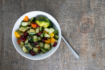 A white ceramic bowl filled with freshly made vegetable ragout with kidney beans on of a wooden rustic table