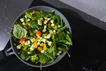 Cooking vegetable ragout with courgettes, peppers, tomatoes, onions, carrots and spinach in a pan on induction stove