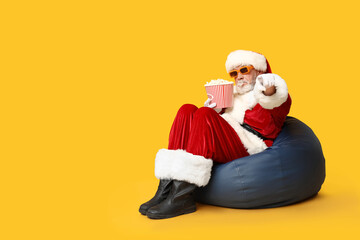 Santa Claus in 3D glasses with bucket of tasty popcorn on yellow background