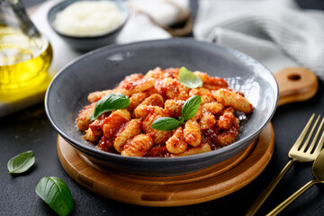 Traditional Italian potato gnocchi with tomato sauce, parmesan cheese and fresh basil leaves on black background