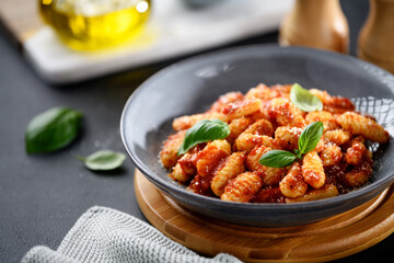 Traditional Italian potato gnocchi with tomato sauce, parmesan cheese and fresh basil leaves on black background