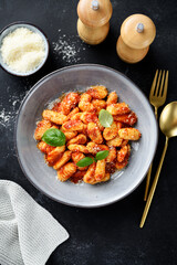 Traditional Italian potato gnocchi with tomato sauce, parmesan cheese and fresh basil leaves on black background, top view