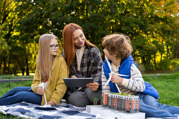 Woman volunteering at camp with children using models of wind turbines and digital tablet