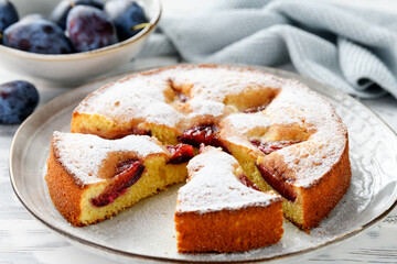 Freshly baked sliced plum ​​pie or cake. White wooden background