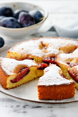 Freshly baked sliced plum ​​pie or cake. White wooden background