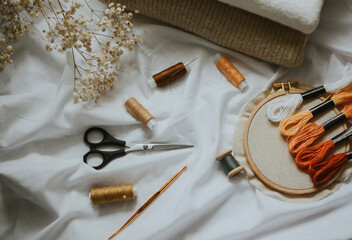 threads of different brown colors with needles, scissors, canvas with floss and measuring tape 