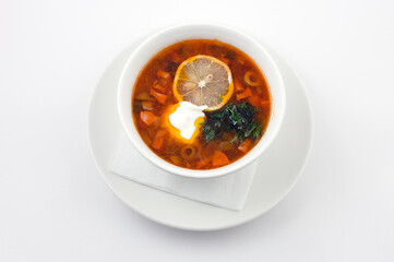 Soup hodgepodge with lemon and sour cream in a white bowl. Top view on white background.