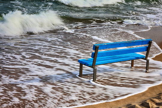 Niebieska ławka na ż&oacute;łtej plaży nad morzem. 