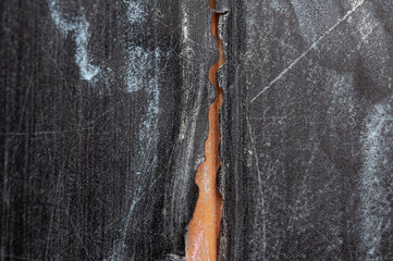 A close-up of a crack in a black surface, showing the underlying brown material