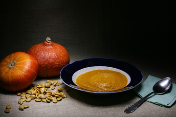 Still life with two red Hokkaido pumpkins, their white seeds and a bowl of pumpkin puree on grey linen