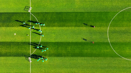 Aerial view of soccer players practicing on a green field. A high-angle shot of a group of soccer players wearing green jerseys during a training session on a well-maintained soccer field. © Iryna