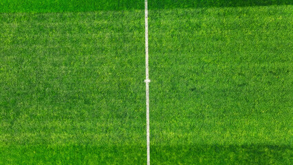Obraz premium Aerial view of a green soccer field with white center line. A high-angle view of a soccer field showcasing the vibrant green grass and the crisp, white center line running across the middle.