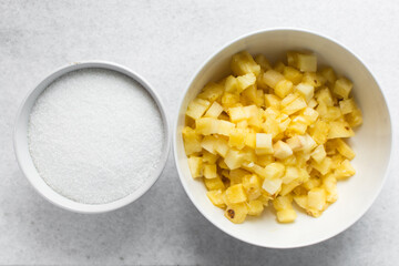 Overhead view of diced pineapple and sugar in white bowls, process of making pineapple cheong or pineapple compote