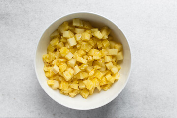 Top view of diced pineapples in a white bowl, overhead view of chopped pineapples on a white background