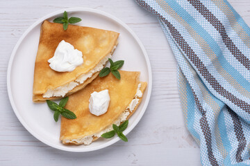 Thin pancakes, russian blini or french crepes with cottage cheese. Tasty homemade breakfast. Top view, copy space