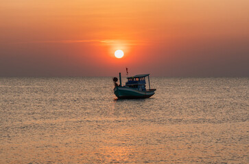 Naklejka premium A scenic sunset at sea with a boat surrounded by calm waters and a fiery sky in the background. The setting sun adds a soft glow to the frame