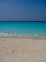 Pristine sandy beach meeting clear, turquoise ocean waves under a bright, cloudless sky. Ideal for travel and summer themes, showcasing nature’s beauty and serene coastal relaxation.