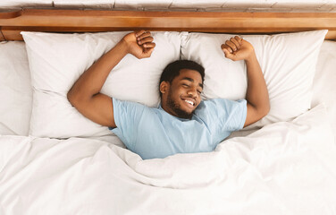 Comfortable sleep. Smiling african-american millennial guy sleeping, sprawled in bed, top view