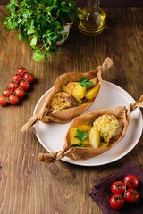 Portioned hearty dinner, baked cutlets with cheese sauce and baked country-style potatoes in a parchment boat shape. Comfort food.