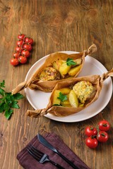 Portioned hearty dinner, baked cutlets with cheese sauce and baked country-style potatoes in a parchment boat shape. Comfort food.