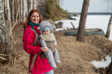 Caucasian red-haired woman walks with her son in an ergo backpack in nature in winter. 