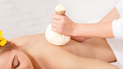 Ayurvedic procedure. Professional doing massage with herbal bags for girl, free space, cropped
