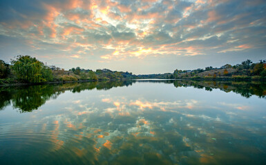 Morning on the river with sunrise and clouds reflections on water,golden sunrise .Old and fallen trees stands on the beach,blue and beautiful water , red and golden sunrise.River at autumn morning.