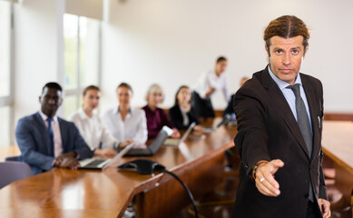 Portrait of successful businessman standing in front of team of businessmen in a meeting room, stretching open hand ready for handshake