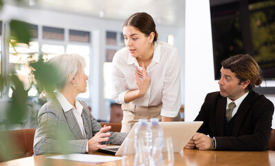 Adult man, elderly woman and young woman in business clothes having meeting in office
