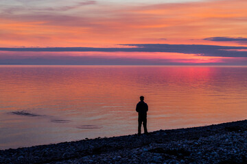 Fototapeta premium Silhouette of a man standing on a pebble beach at sunset