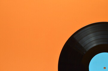one quarter of an old black vinyl record with blank cyan label on the edge of orange background