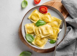Homemade ravioli pasta with cheese, tomatoes and basil in a plate on a wooden board on a light  background
