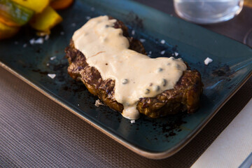 Tasty veal steak with pepper sauce and baked potatoes at plate with carrot