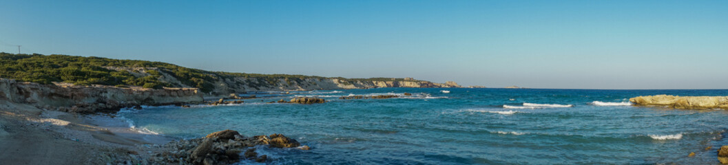 Fototapeta premium Serenity at the shoreline: tranquil waves caress a sunlit rocky beach on a beautiful afternoon.