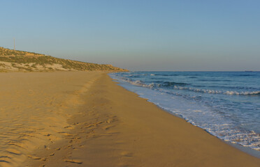 Tranquil beach shoreline at sunset reflecting golden hues and gentle waves lapping the sand.