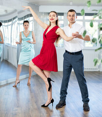 Fototapeta premium Guy and girl in stage costumes, under guidance of mentor, practice tango in choreographic studio. Ballet dancers during personal training session. Professional rendering of dance entertainment