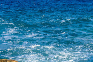 Waves crash gently against the shore under a bright, clear sky on a sunny day by the ocean.