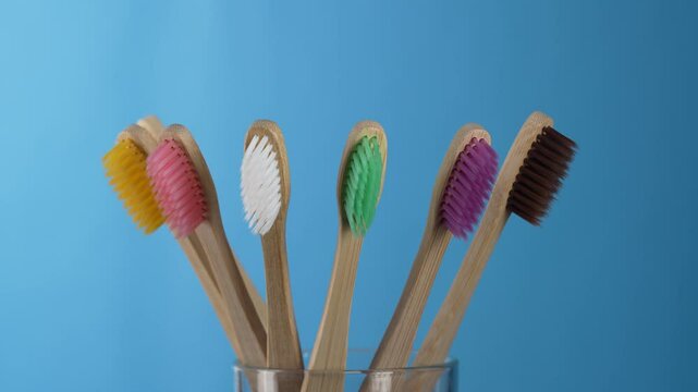 Set of colorful bamboo toothbrushes in glass on blue background, close up, rotates. Zero waste, plastic free, eco friendly organic product concept