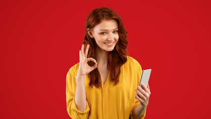 Naklejka premium Great Mobile App. Millennial Girl Using Smartphone Gesturing Okay Posing On Green Studio Background. Panorama