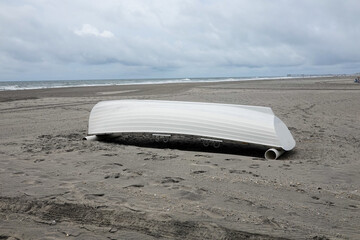 White row boat upside down on a gray sandy deserted beach by the ocean